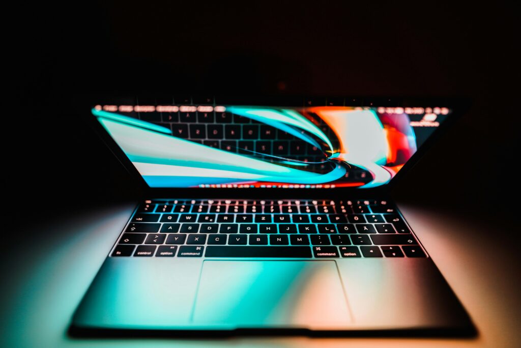 Open laptop with a colorful display reflecting on its keyboard, set against a dark background.