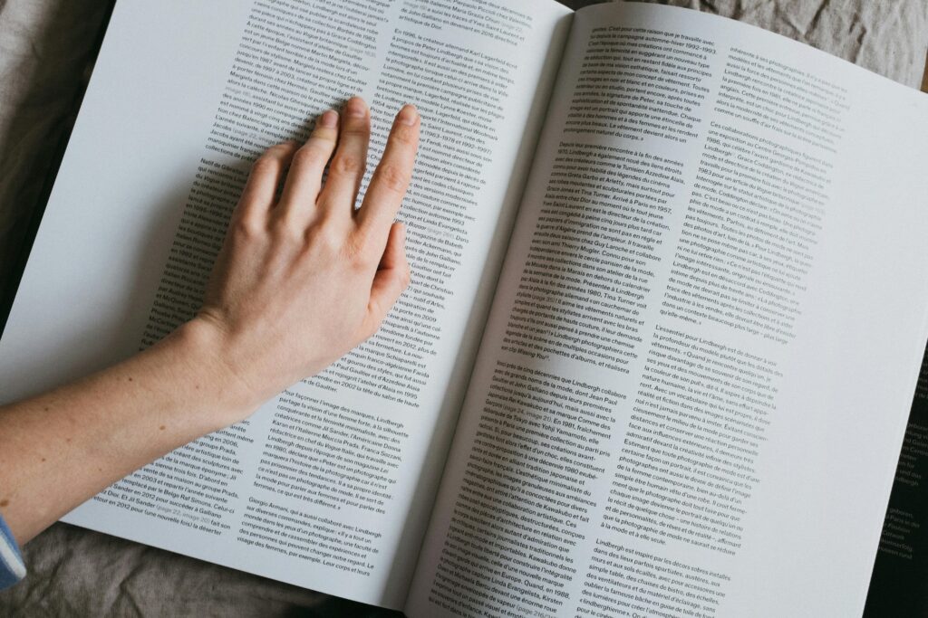 From above of crop anonymous female searching for information in article of book