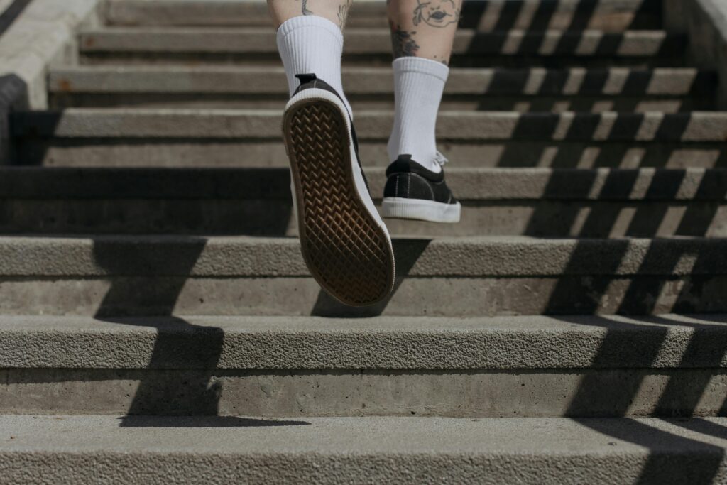 Athletic person wearing black sneakers and white socks jogging up concrete stairs outdoors.