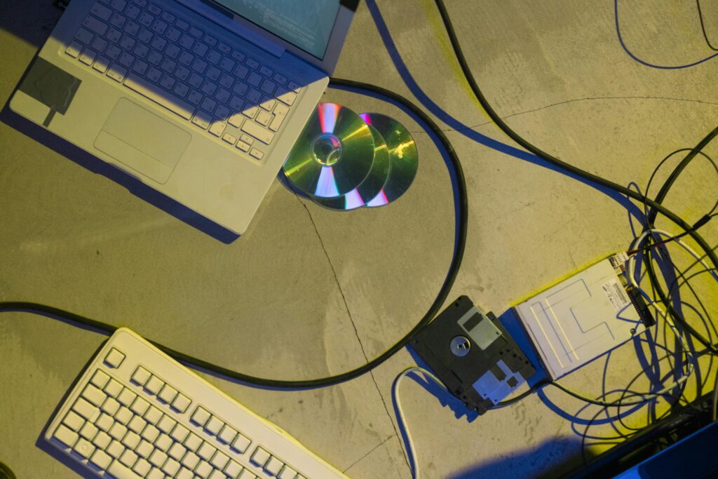 Flat lay of vintage laptop, CDs, floppy disk, and wires suggest a retro tech theme.