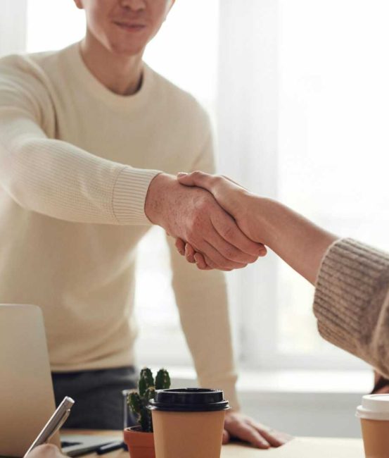 Close-up of professionals shaking hands over coffee in a modern office.