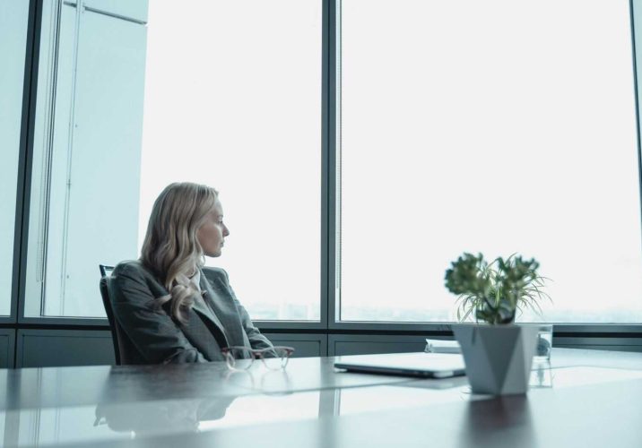 A businesswoman in a suit looking out the window of a contemporary office with a modern setup.