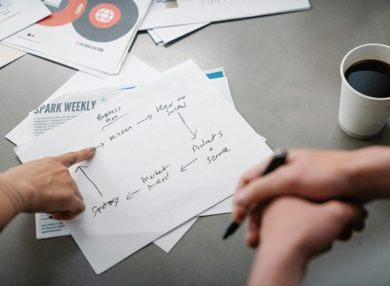 Hands pointing at a handwritten business strategy diagram over coffee.