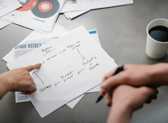 Hands pointing at a handwritten business strategy diagram over coffee.